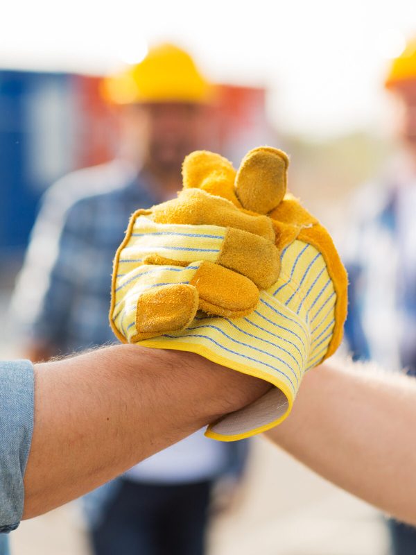 building, teamwork, partnership, gesture and people concept - close up of builders hands in gloves greeting each other with handshake on construction site